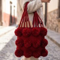 Bolsa tote artesanal tejida en telar de cintura con pompones de algodón.